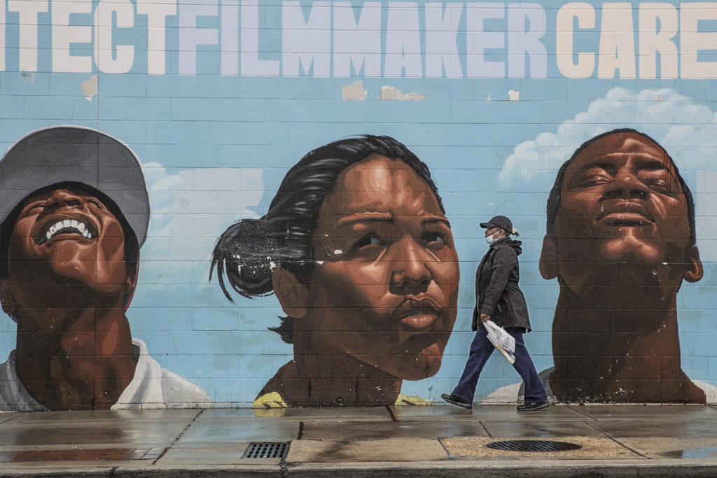 Virus Outbreak Philadelphia A woman wearing a surgical mask makes her way past a mural on the west side of the Save-A-Lot store at 22nd and Lehigh. (Michael Bryant/The Philadelphia Inquirer via AP)