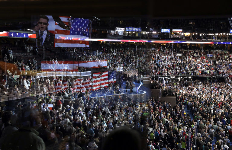 The stage is reflected on a glass window on the suite level at Wells Fargo Arena as Timmy Kelly sings the national anthem before the start of the second day session of the Democratic National Convention in Philadelphia, in 2016.  (John Locher/AP Photo, File)