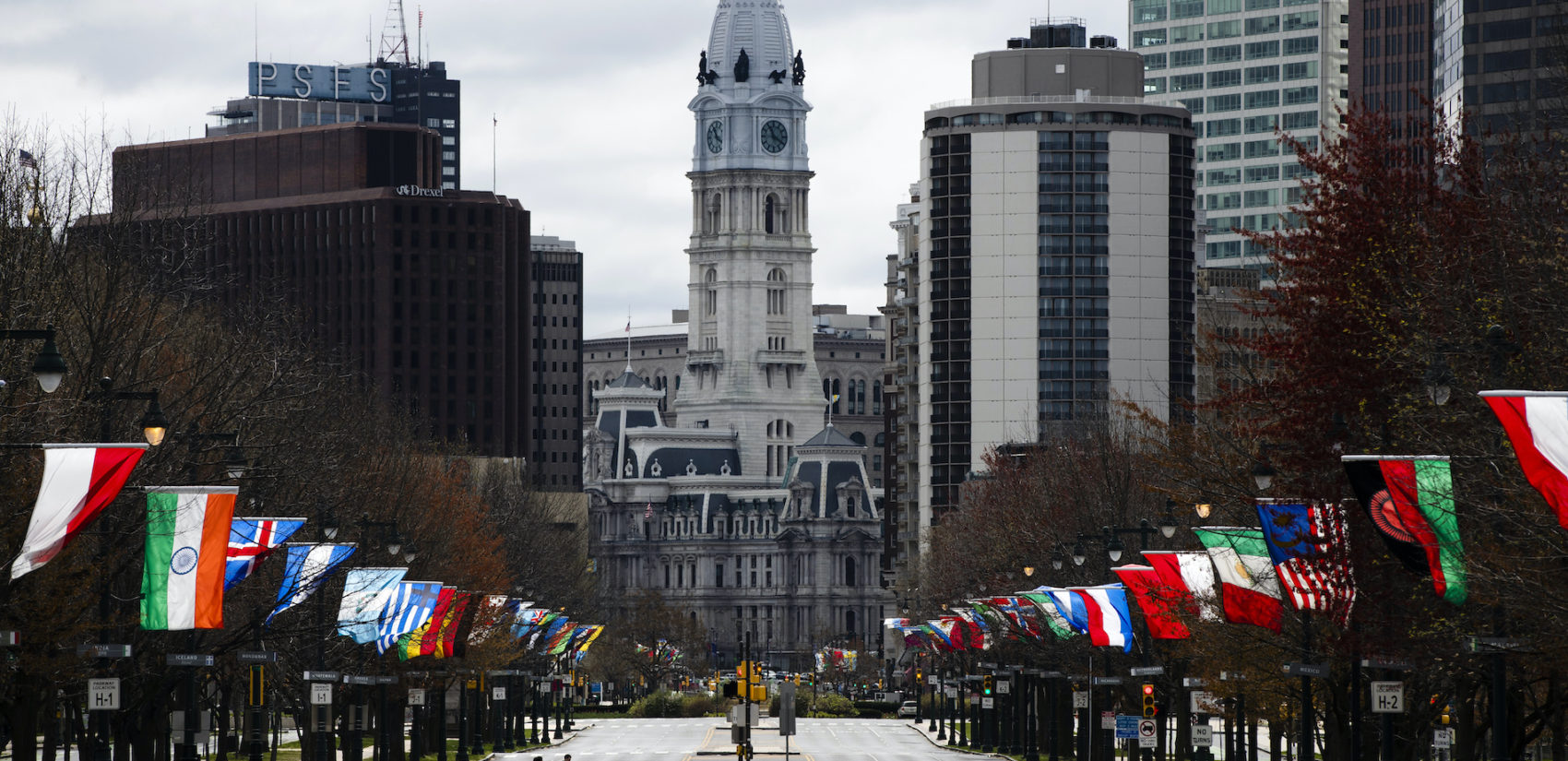 Flags from different countries blow in the wind as City Hall is visible in the background.