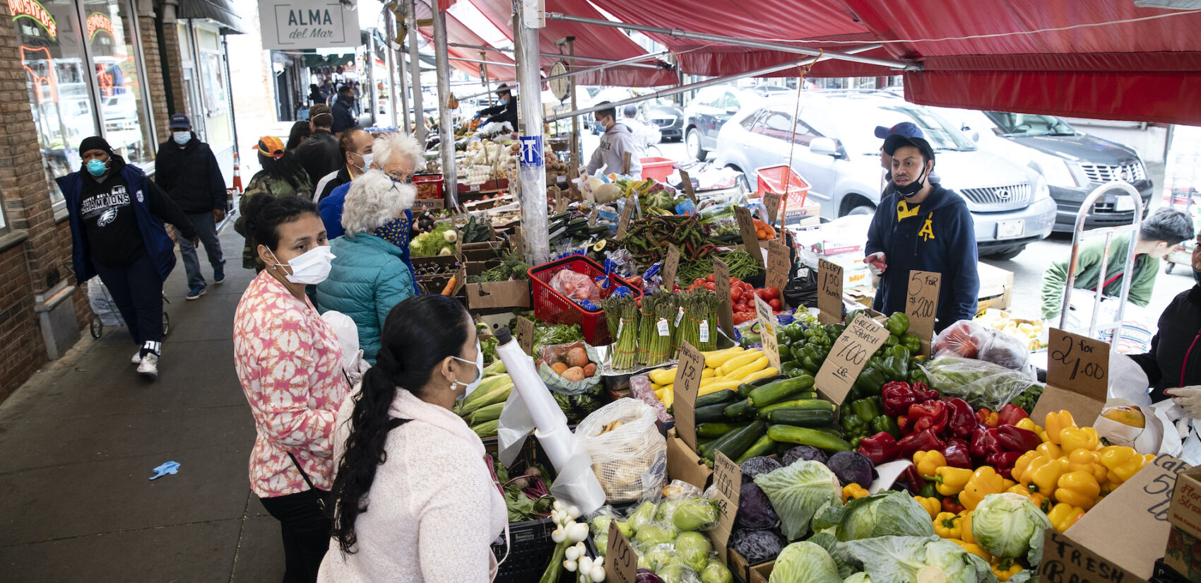 Customers wearing face coverings to protect against the spread of the coronavirus, shop at a produce stand on South 9th Street in the Italian Market neighborhood of Philadelphia, Thursday, April 9, 2020. (AP Photo/Matt Rourke)