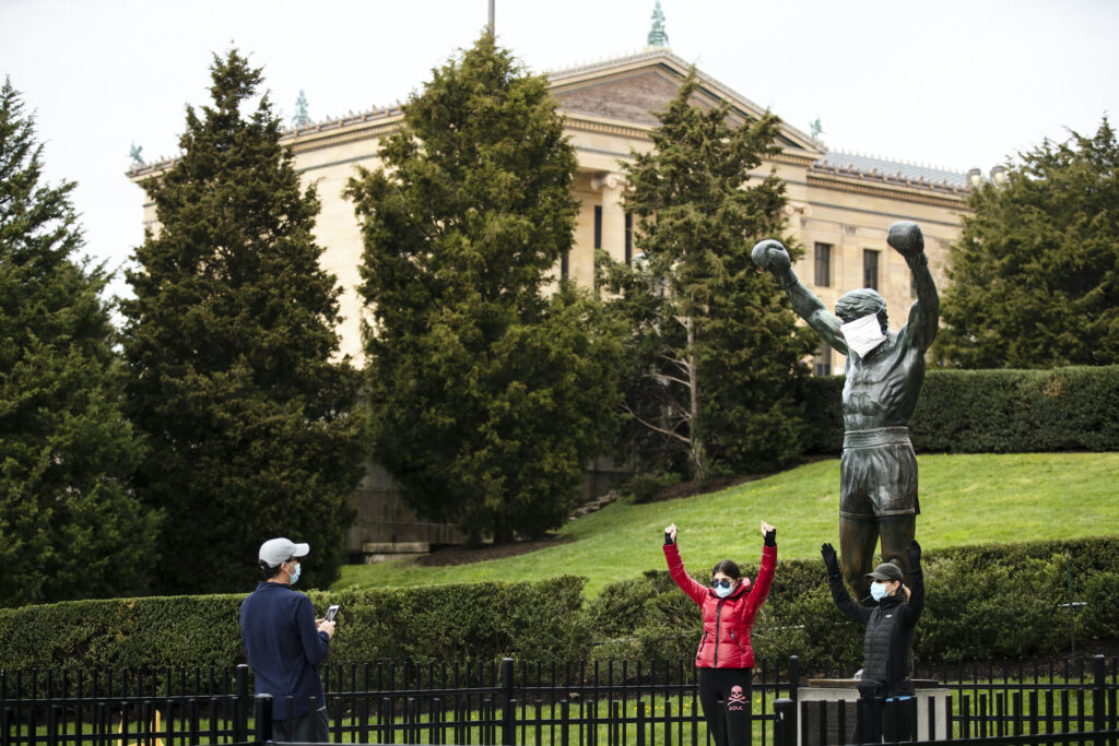 Virus Outbreak Pennsylvania Daily Life People wearing a protective face masks as a precaution against the coronavirus take photos with the Rocky statue outfitted with mock surgical face mask at the Philadelphia Art Museum in Philadelphia, Tuesday, April 14, 2020. (AP Photo/Matt Rourke)