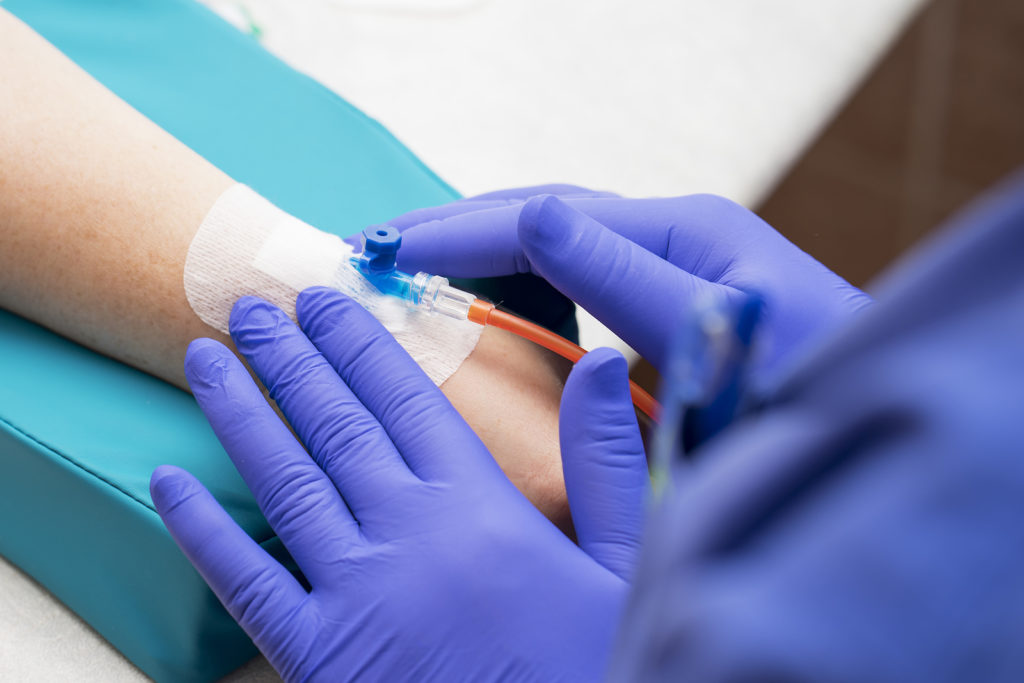 Medical Nurse With Blue Latex Gloves Inputs Catheter To Vein Pat (MKrivonos/BigStock)