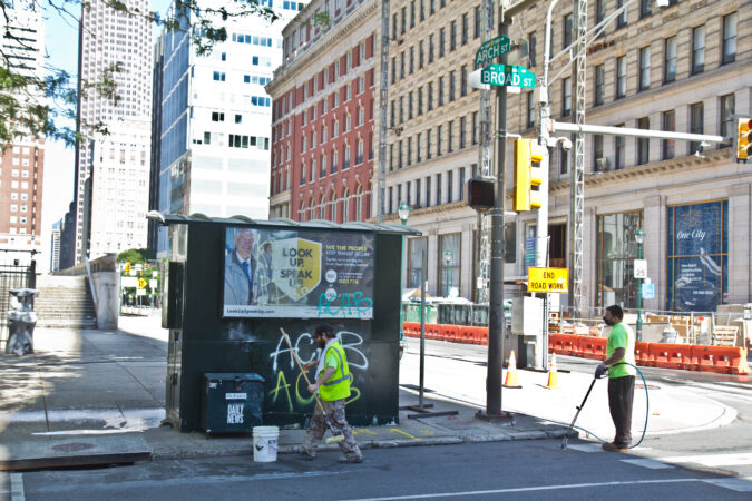 Clip workers scrub graffiti off a newsstand at Broad and Arch Streets in Philadelphia. (Kimberly Paynter/WHYY)