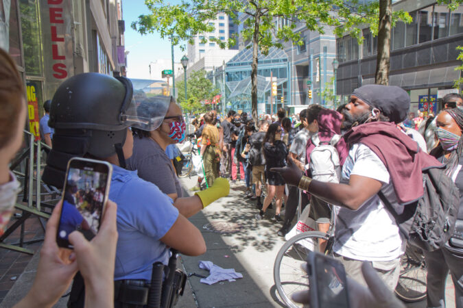A woman argues with a man in from of a Modell’s Sporting Goods Store after people tried to run off with more merchandise in Center City Philadelphia while officers stand by in riot gear. (Kimberly Paynter/WHYY)