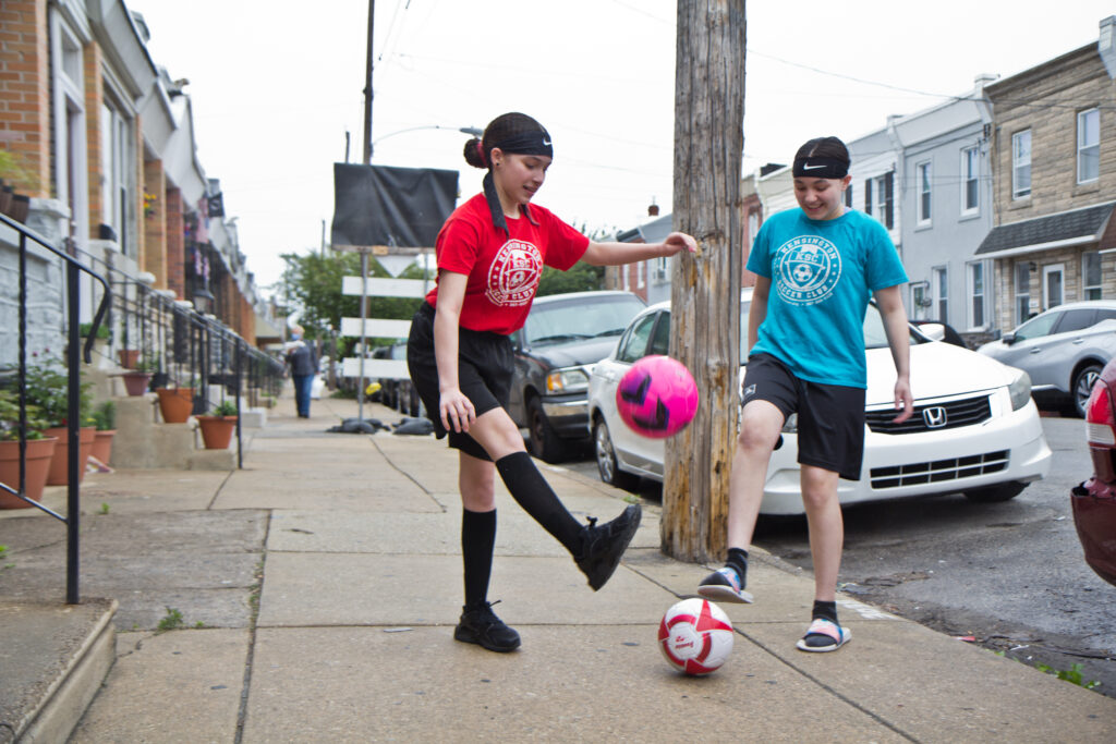 2020 5 8 k paynter soccer Yvanna, 13, (right), and Emilia, 12, (left) play with soccer balls on their block. (Kimberly Paynter/WHYY)