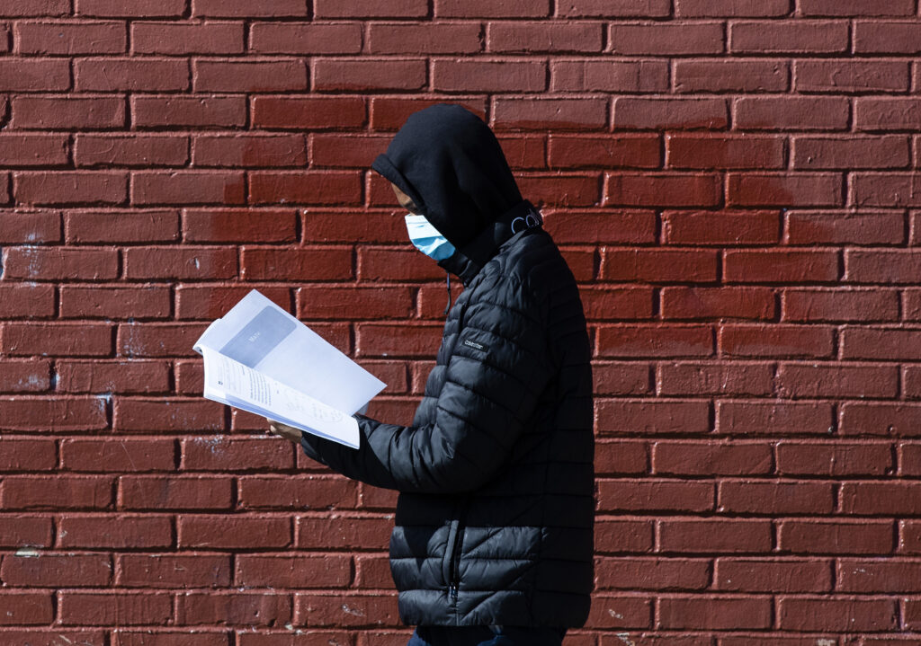 Virus Outbreak Digital Divide In this Thursday, March 26, 2020, photo, Terrell Bell, wearing a protective face mask, looks at a learning guide he picked up for his little sister at John H. Webster Elementary School in Philadelphia. (AP Photo/Matt Rourke)