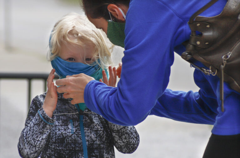 Bridget Kreider, right, helps her three-year-old daughter Maggie pull on her protective face covering before entering a store, Wednesday, May 20, 2020, in Harmony, Pa. Customers entering stores are required to wear face coverings to help prevent the spread of the new coronavirus during the COVID-19 pandemic under the state yellow phase reopening guide. (AP Photo/Keith Srakocic)
