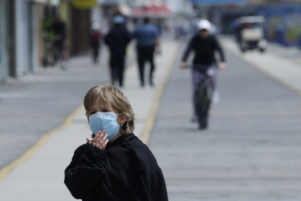 Virus Outbreak New Jersey Beaches A boy adjusts his mask as he walks down the boardwalk, Thursday, May 21, 2020 in Wildwood, N.J. (AP Photo/Matt Slocum)