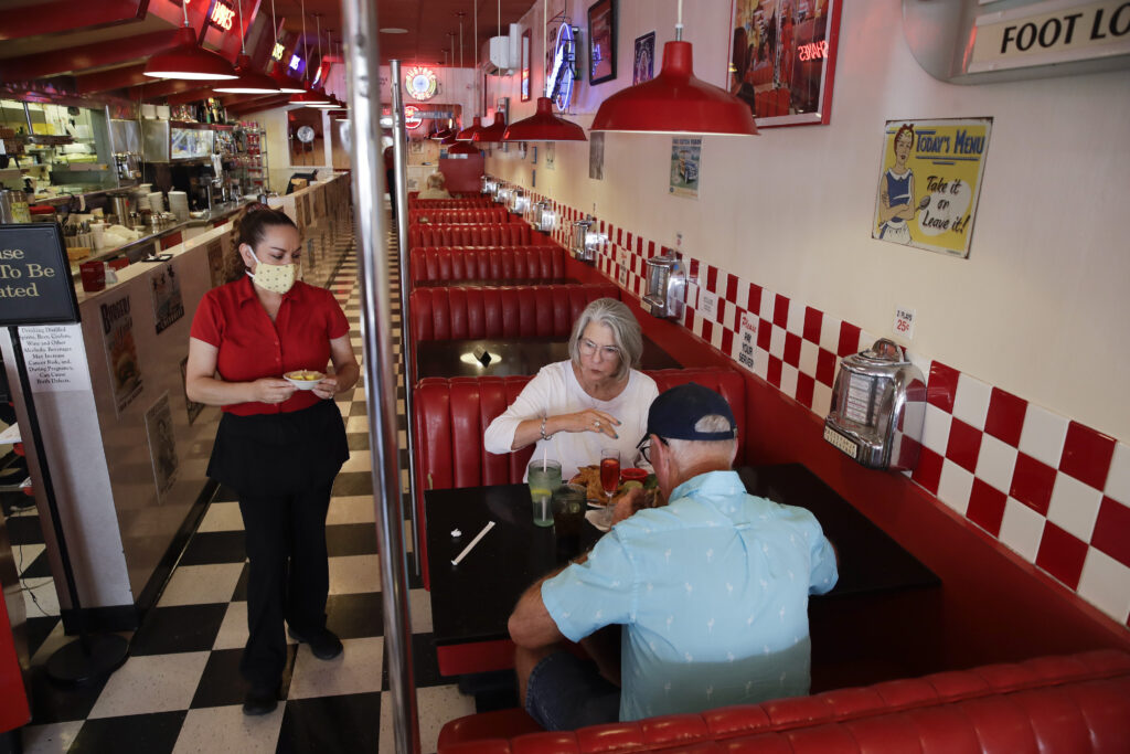 Lynn Tanner, Ryan Tanner Lynn Tanner, center, and her husband Ryan, bottom right, are served lunch at Busy Bee Cafe Thursday, May 21, 2020, in Ventura, Calif. Much of the country remains unlikely to venture out to bars, restaurants, theaters or gyms anytime soon, despite state and local officials increasingly allowing businesses to reopen. That's according to a new survey by The Associated Press-NORC Center for Public Affairs Research. (AP Photo/Marcio Jose Sanchez)