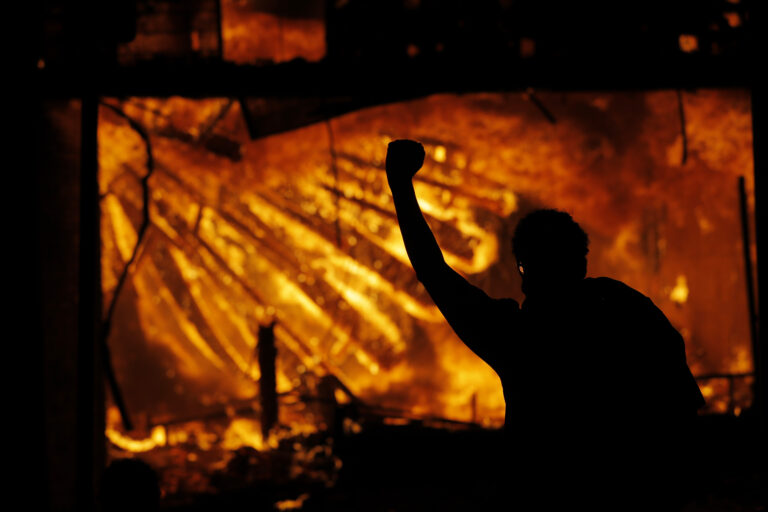 A protester gestures in front of the burning 3rd Precinct building of the Minneapolis Police Department on Thursday, May 28, 2020, in Minneapolis. (AP Photo/Julio Cortez)