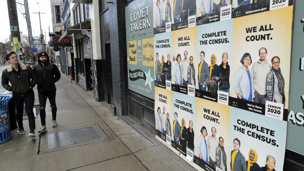 People walk past posters encouraging participation in the 2020 census in April in Seattle. A group of House Democrats have introduced a bill that would grant the U.S. Census Bureau's request to delay major deadlines for delivering results of the count because of the pandemic. (Ted S. Warren/AP Photo)