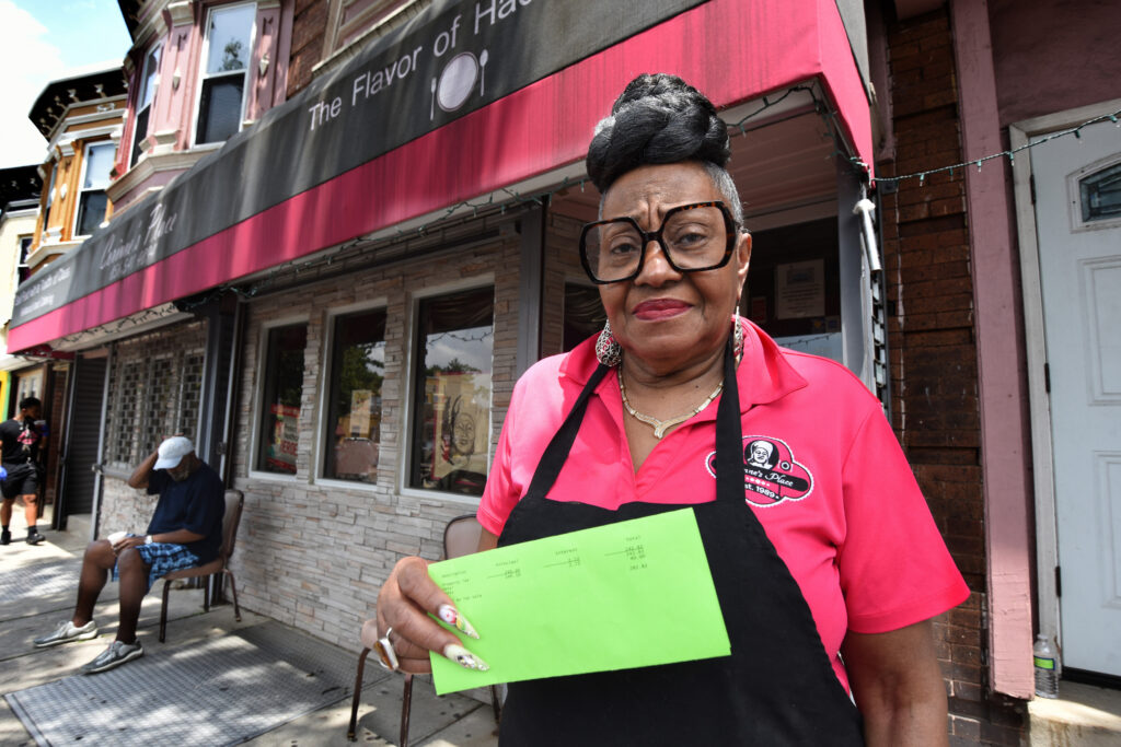 01-1 On June 5, Corinne Bradley-Powers, owner of Corinne's Place, stands in front of her popular Camden restaurant holding the notice she received that her restaurant would be on a list for sheriff's sale this month if she didn't pay the $282 she owed. (Photo by April Saul for WHYY)