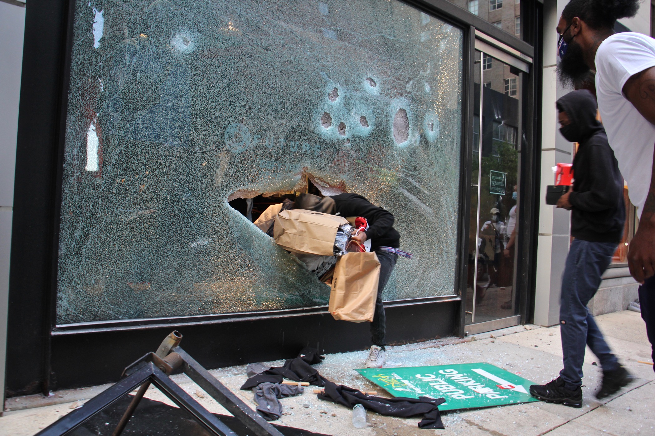 A looter emerges from the shattered window of a North Face store
