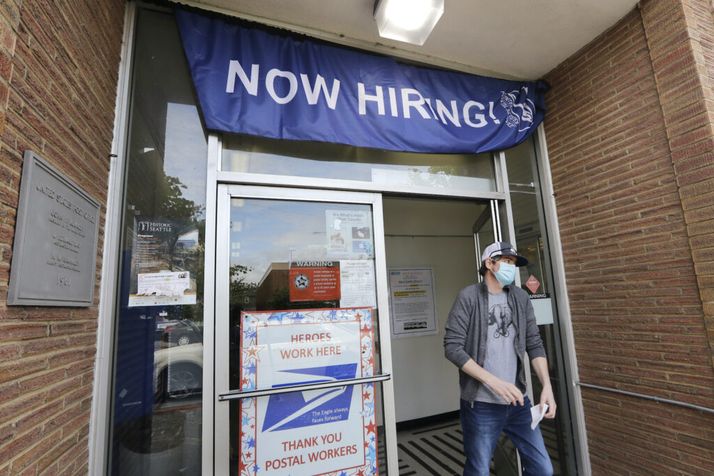 Economy Jobs Report A customer walks out of a U.S. Post Office branch and under a banner advertising a job opening