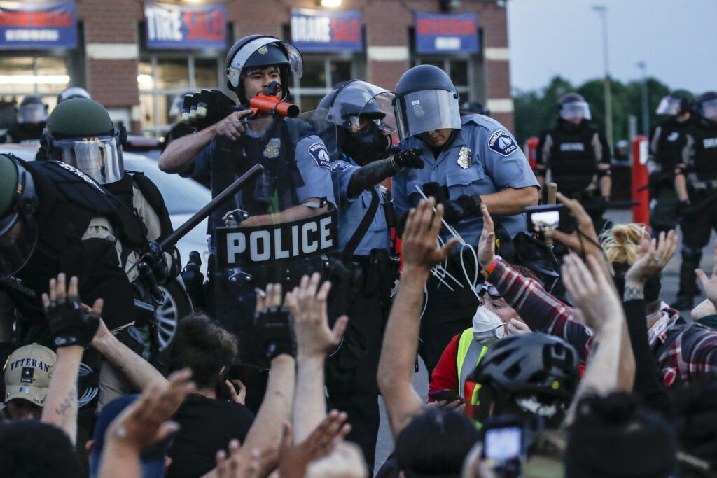 Protests Origins A police officer points a hand cannon at protesters who have been detained pending arrest on South Washington Street, Sunday, May 31, 2020, in Minneapolis. (AP Photo/John Minchillo)