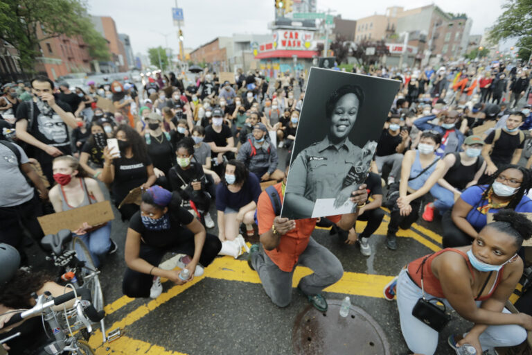 A man holds a photograph of Breonna Taylor on her birthday as he kneels with other protesters