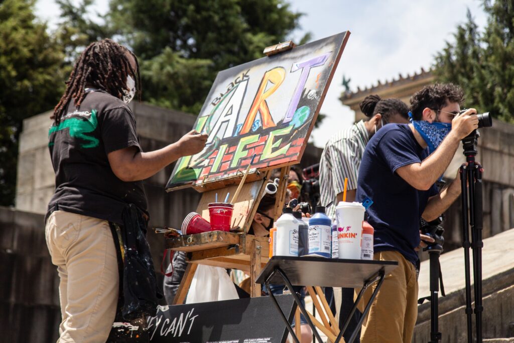 Artist Keisha Whatley paints on the steps of the Art Museum at a rally demanding funding for the arts in Philadelphia. (Kimberly Paynter/WHYY)