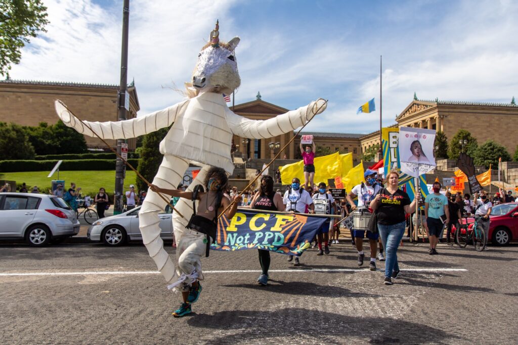 Image from iOS (85) Samantha Rise leads a march demanding arts funding in a giant unicorn puppet