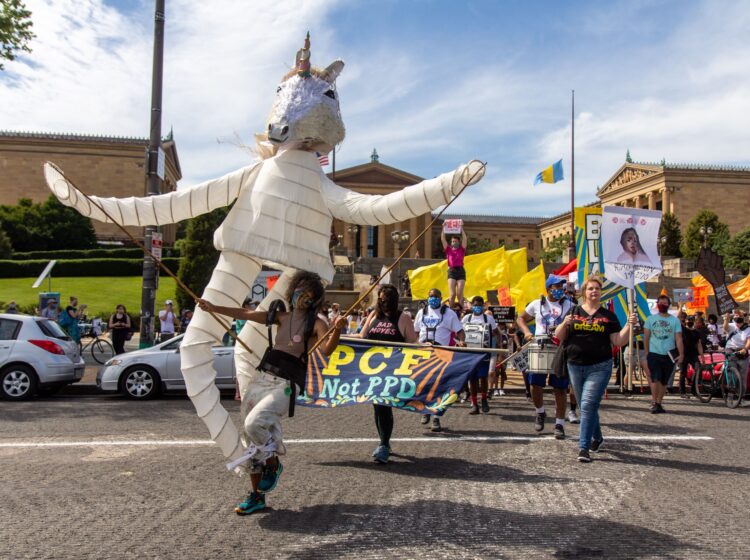 Samantha Rise leads a march demanding arts funding in a giant unicorn puppet