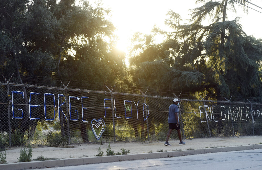 A walker passes by the names of George Floyd and Eric Garner spelled out in fabric at the art installation “Say Their Names: Silver Lake Memorial” at the Silver Lake Reservoir, on June 9, in Los Angeles. There has been a recent push for a nationwide ban on police chokeholds following George Floyd’s death. A walker passes by the names of George Floyd and Eric Garner spelled out in fabric at the art installation