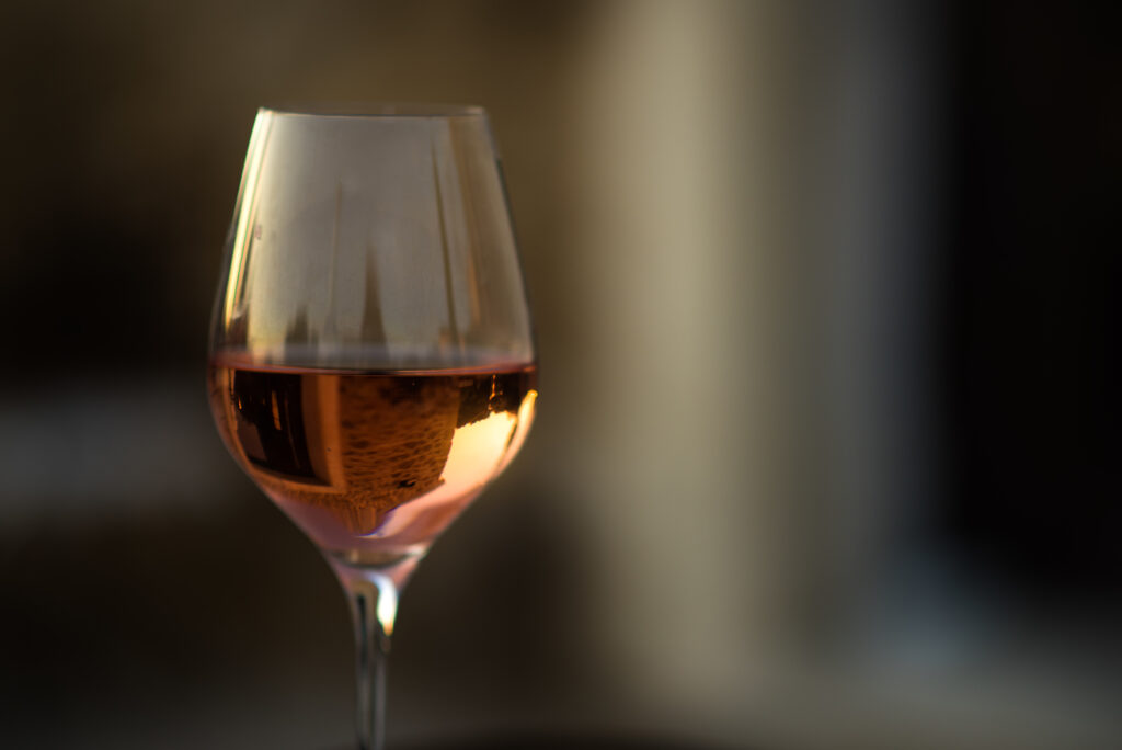 Picture In Low Key Of Glass Of Rose Wine With Reflection Of Old Picture in low key of glass of rose wine with reflection of old stone traditional provencal house in it. Rose wine in Provence, France. Light alcoholic drink.