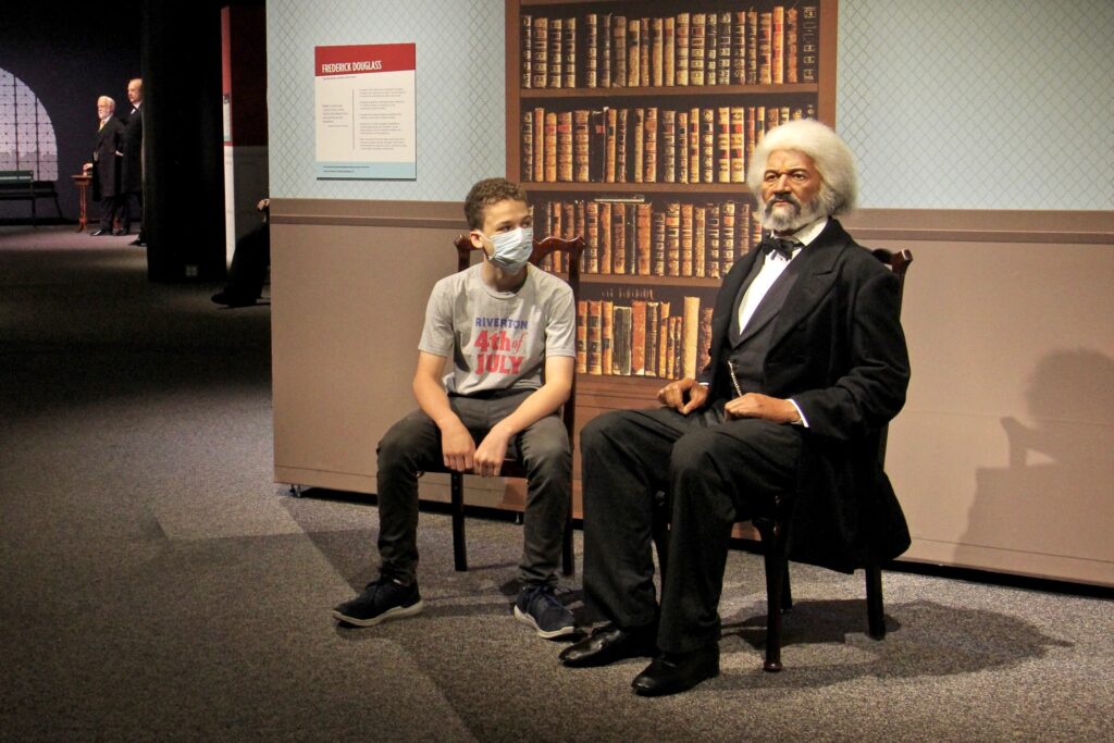 2020 07 08-e lee-caleb cattell-philadelphia franklin institute-reopening the presidents by madame tussauds Caleb Cattell takes a seat beside a wax figure of Frederick Douglass at the Franklin Institute. The 13-year-old from Riverton, N.J., and his family were among the first wave of visitors when the Institute reopened on Wednesday. (Emma Lee/WHYY)