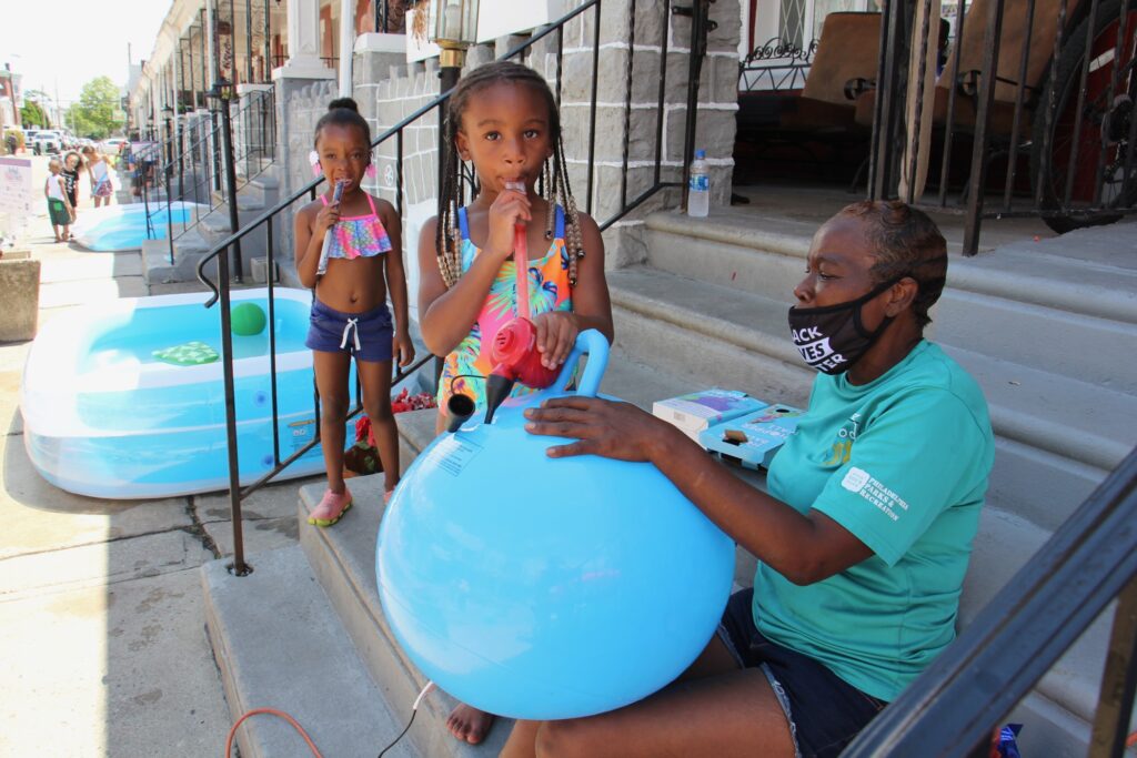 2020 07 13-e lee-roslyn myers-philadelphia 5800 delancey street-playstreets Taylor Corbin, 4, (center) helps block captain Roslyn Myers inflate a hopper ball