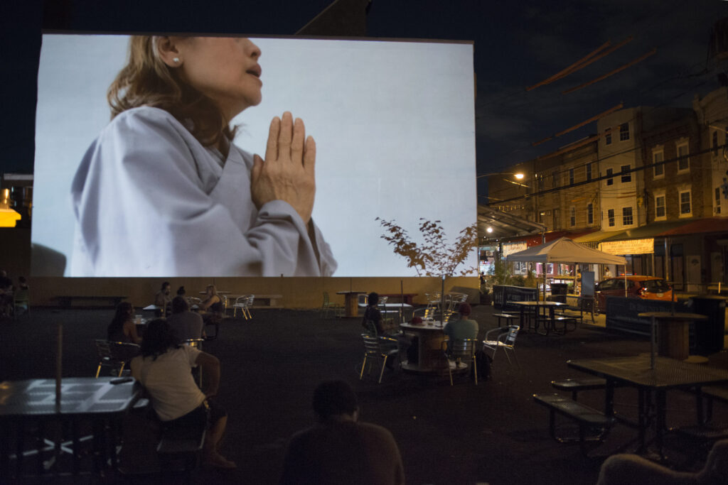 20200711-Cleanse_LW-0755 A woman holds her hands in a prayer position in the video by Kevin Nguyen projected during the 'Cleanse' exhibit in the Italian Market on July 11, 2020. (Photo by Lori Waselchuk)