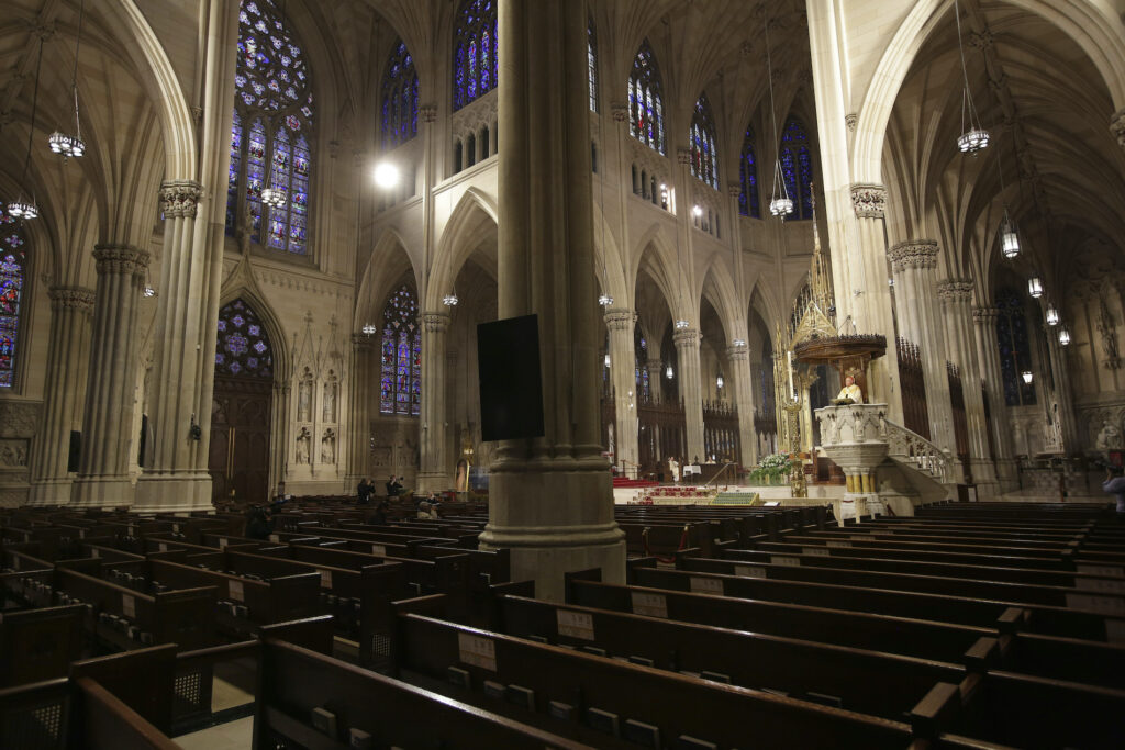 In this Sunday, April 12, 2020 file photo, Archbishop Timothy Dolan, right, delivers his homily over mostly empty pews as he leads an Easter Mass at St. Patrick's Cathedral in New York. (AP Photo/Seth Wenig)