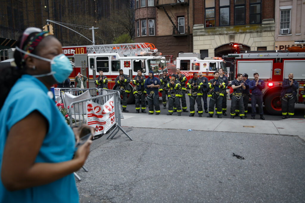 Virus Outbreak Workers Comp FDNY firefighters gather to applaud medical workers as attending physician Mollie Williams, left, wears personal protective equipment due to COVID-19 concerns outside Brooklyn Hospital Center, Tuesday, April 14, 2020, in New York. (AP Photo/John Minchillo)