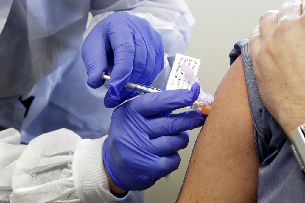Virus Outbreak Vaccine Race In this March 16, 2020, file photo, a subject receives a shot in the first-stage safety study clinical trial of a potential vaccine by Moderna for COVID-19, the disease caused by the new coronavirus, at the Kaiser Permanente Washington Health Research Institute in Seattle. (AP Photo/Ted S. Warren)