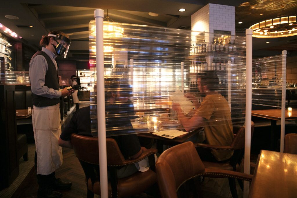 Virus Outbreak Unemployment Benefits In this June 22, 2020, file photo, wearing a face shield, server Brandon Fricke, left, takes orders from dine-in customers surrounded by protective dividers at Water Grill seafood restaurant in Los Angeles. (AP Photo/Jae C. Hong)