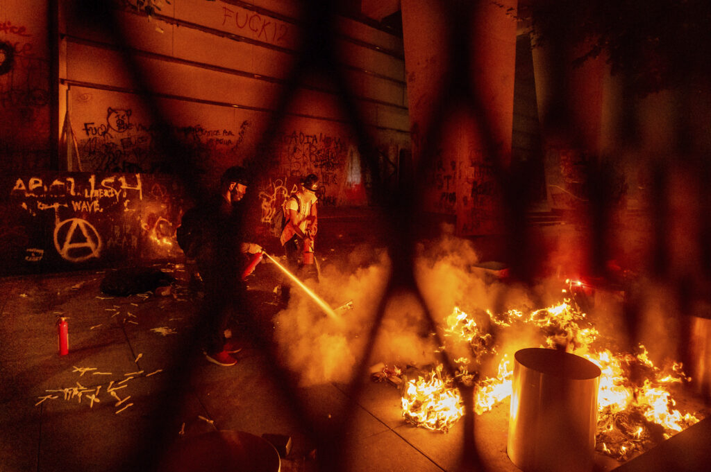 Racial Injustice Portland A protester extinguishes a fire set by fellow protesters at the Mark O. Hatfield United States Courthouse on Wednesday, July 22, 2020, in Portland, Ore. (AP Photo/Noah Berger)