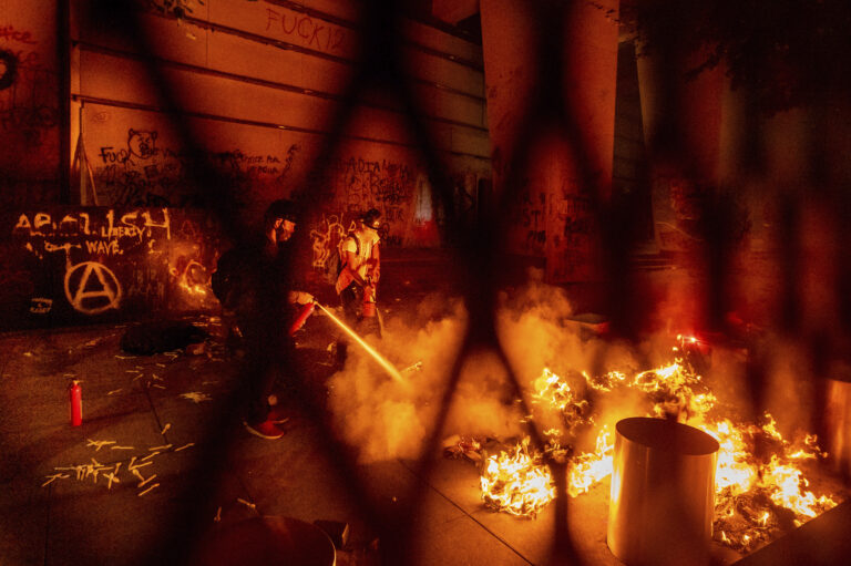 A protester extinguishes a fire set by fellow protesters at the Mark O. Hatfield United States Courthouse on Wednesday, July 22, 2020, in Portland, Ore. (AP Photo/Noah Berger)