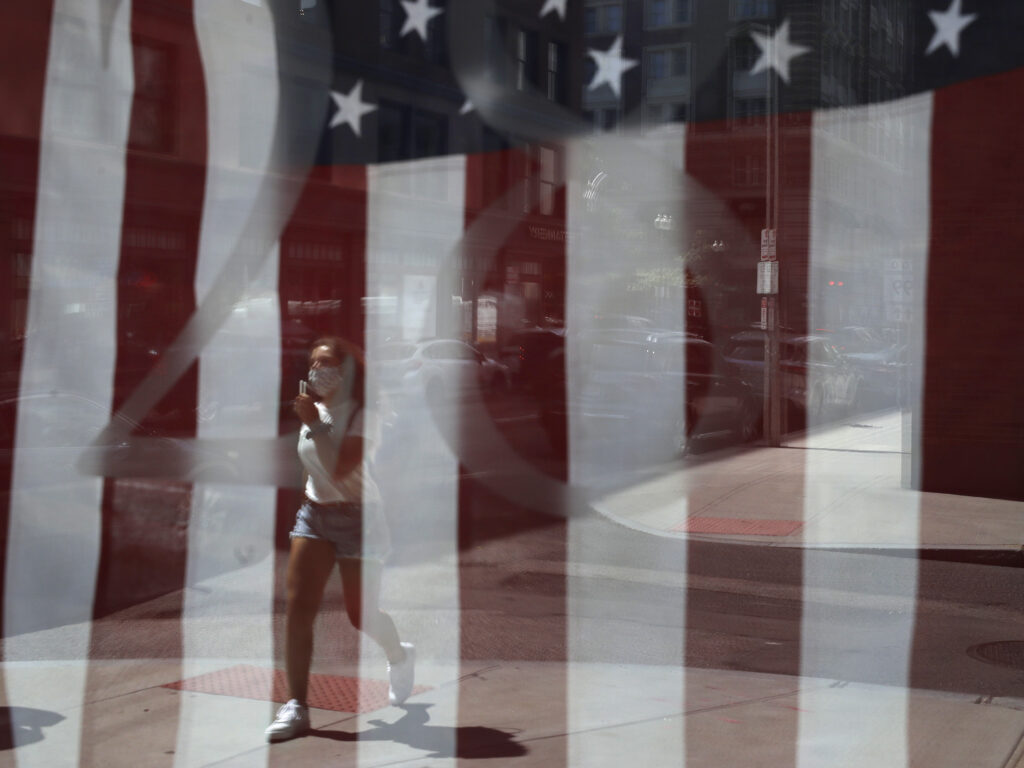 A passerby wears a mask out of concern for the coronavirus while walking past an American flag displayed in Boston on Tuesday. The U.S. has now recorded more than 3 million confirmed cases of the coronavirus. A passerby wears a mask out of concern for the coronavirus while walking past an American flag displayed in Boston on Tuesday. The U.S. has now recorded more than 3 million confirmed cases of the coronavirus.