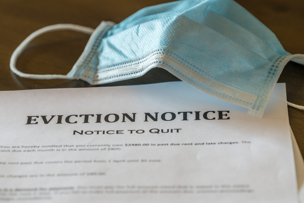Defaulting Renter With Facemask Receives Letter Giving Notice Of Defaulting renter with face mask receives letter giving notice of eviction from home on wooden table. (BackyardProductions/BigStock)