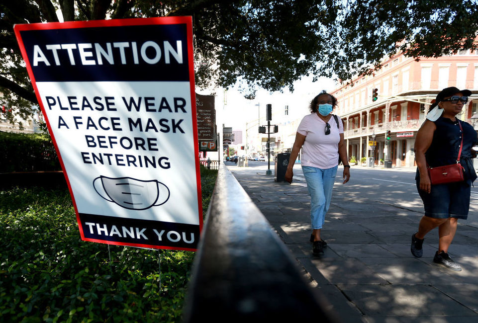 Scientists estimate that near-universal mask use could make a major difference in bringing down coronavirus infections in the United States. Visitors walk past face mask signs along Decatur Street