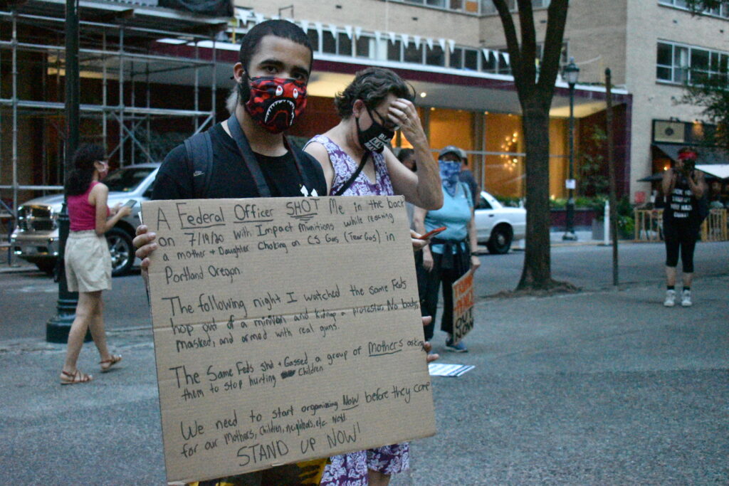 Jordan Johnson holds a sign detailing a recent incident with what he says were federal police in Portland, Oregon. (Brett Sholtis/WITF)