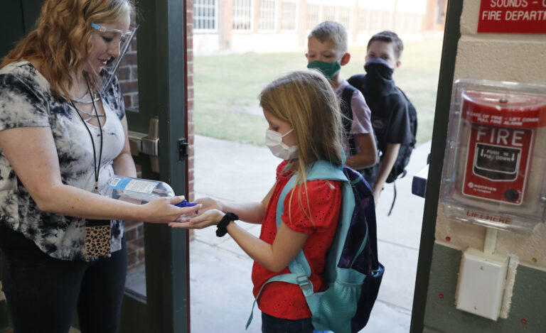 In this Aug. 5, 2020, file photo, wearing masks to prevent the spread of COVID-19, elementary school students use hand sanitizer before entering school for classes in Godley, Texas. (AP Photo/LM Otero)