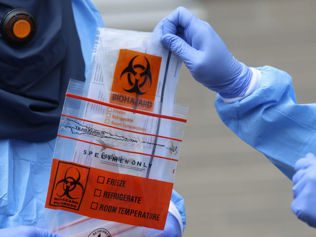 A COVID-19 test is collected in Salt Lake City, Utah. A federal study published Monday found that Hispanic and non-white workers make up a disproportionate share of COVID-19 cases associated with workplace outbreaks in Utah. In this May 14, 2020, photo, Salt Lake County Health Department public health nurse Lee Cherie Booth performs a COVID-19 test outside the Salt Lake County health department, in Salt Lake City. People who test positive are logged into an online database and assigned as new case to contract tracers at the health department who call them to find out who they've been around and where they've been. (AP Photo/Rick Bowmer)