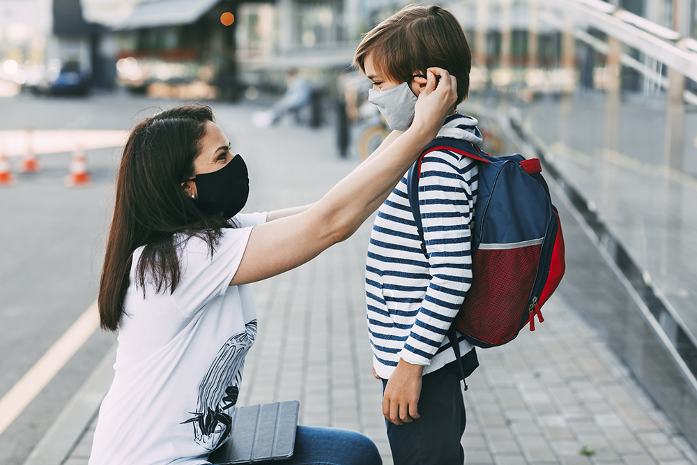 Mother Adjusts Her Sons Mask. A Mother And Child On Their Way To A mother wearing a face mask adjusting a face mask on her son before he goes to school