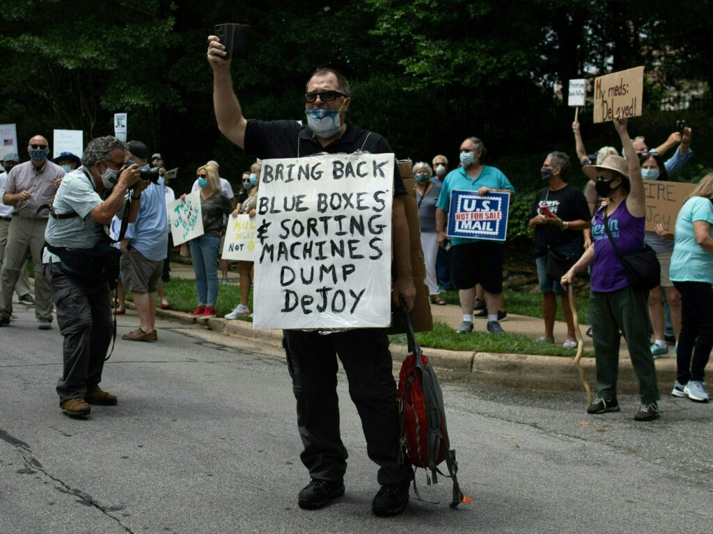 A group of protestors holds a demonstration in front of Postmaster General Louis DeJoy’s home in Greensboro, N.C. on Sunday. DeJoy has recently come under fire for changes made at the U.S. Postal Service that have delayed mail in advance of the November elections. A group of protestors holds a demonstration in front of Postmaster General Louis DeJoy's home in Greensboro, N.C. on Sunday. DeJoy has recently come under fire for changes made at the U.S. Postal Service that have delayed mail in advance of the November elections.