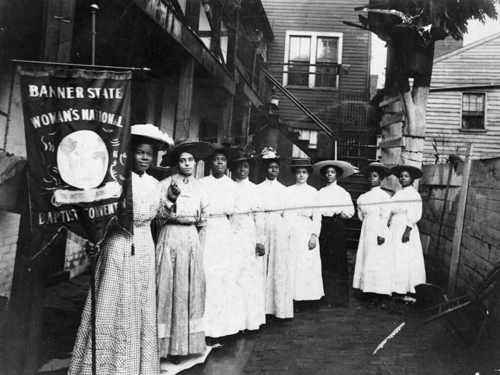 Nannie Helen Burroughs holds a banner reading, “Banner State Woman’s National Baptist Convention” as she stands with other African American women, photographed between 1905 and 1915. Burroughs was an educator and activist who advocated for greater civil rights for African Americans and women. Nannie Helen Burroughs holds a banner reading,