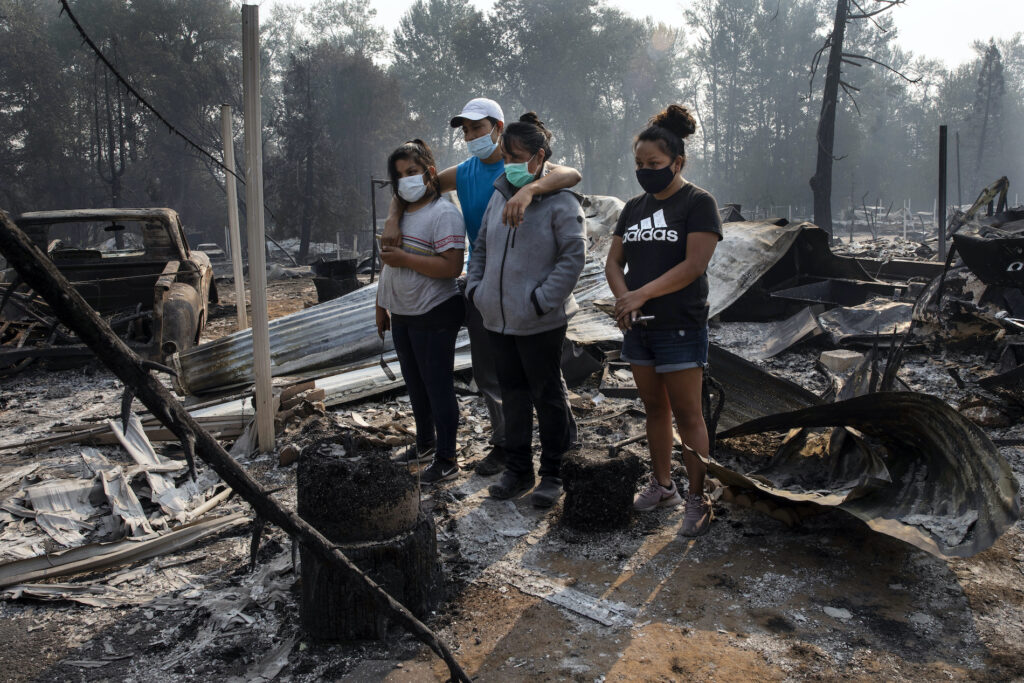 The Reyes family looks at the destruction of their trailer at the Coleman Creek Estates where 121 trailers burned as wild fires devastate the region on Thursday in Portland, Ore. The Reyes family lived in the park for 20 years. (AP Photo/Paula Bronstein)