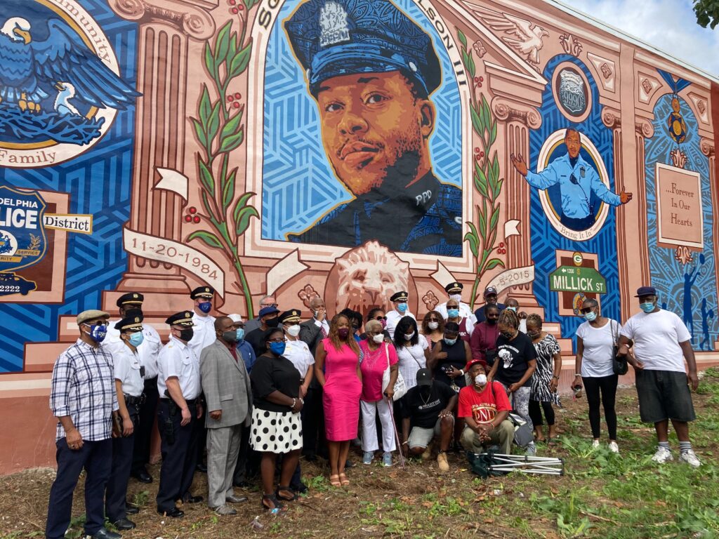 PPD_sgt_wilson_mural_HC_090120_01 City officials, police officers from the 18th district, and neighborhood residents pose in front of the Sgt. Robert Wilson III mural