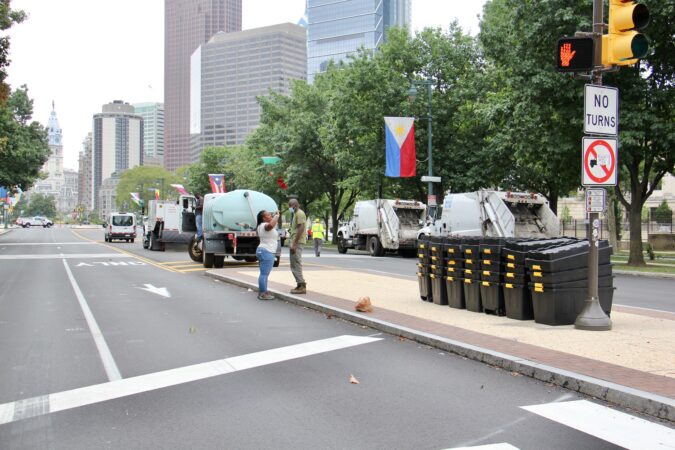 City workers with garbage trucks and bins for possessions wait on the Ben Franklin Parkway