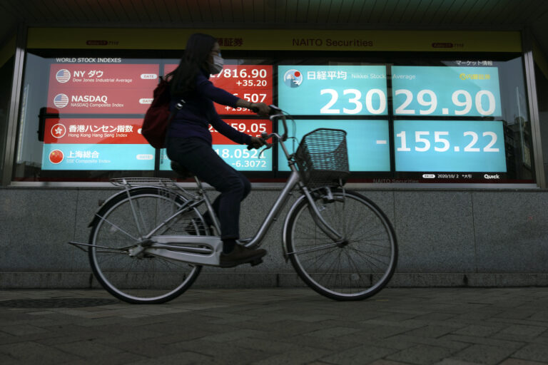 A woman rides a bicycle  past an electronic stock board showing Japan's Nikkei 225 index at a securities firm in Tokyo Friday, Oct. 2, 2020. (AP Photo/Eugene Hoshiko)