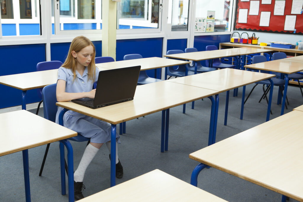 A student uses a laptop in an empty classroom. A student uses a laptop in an empty classroom.