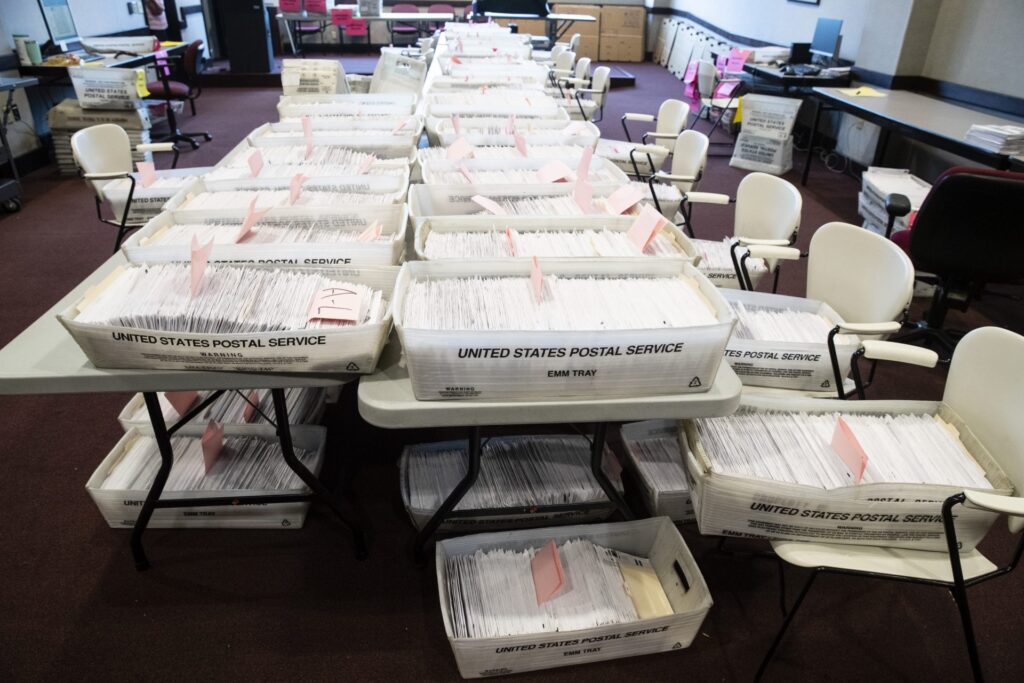 AP_20149750775821-1920×1280 A table full of boxes of mail-in ballots is visible.