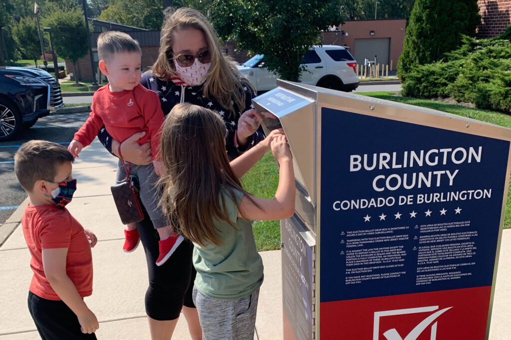 Nicole Flaherty, top, stands with her kids as her 7-year old daughter Madelyn places the ballot in the box in the Burlington County ballot box
